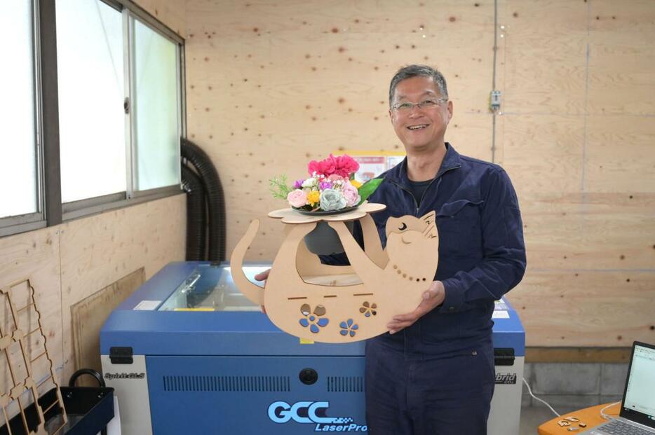 木製フラワースタンド「ゆらりん」を持つ同社社長の松田忠明さん