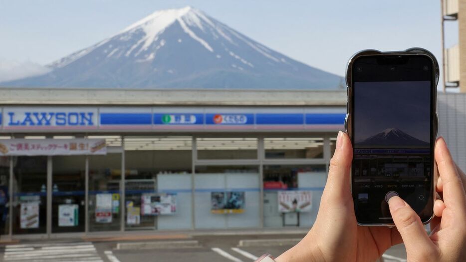 コンビニの向こう側に見える富士山。人気撮影スポットとして外国人観光客が殺到、現在は撮影防止の黒い幕が張られている＝2024年5月、山梨県富士河口湖町（ロイター）