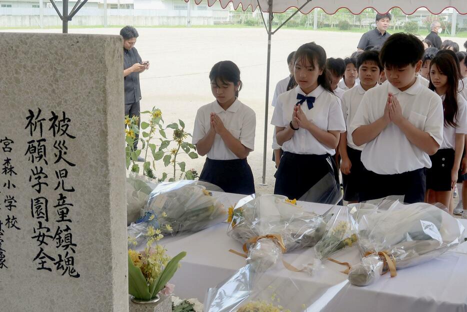 米軍機墜落事故の犠牲者の名前が刻まれた「仲よし地蔵」に手を合わせる子どもたち＝30日午前、沖縄県うるま市の宮森小