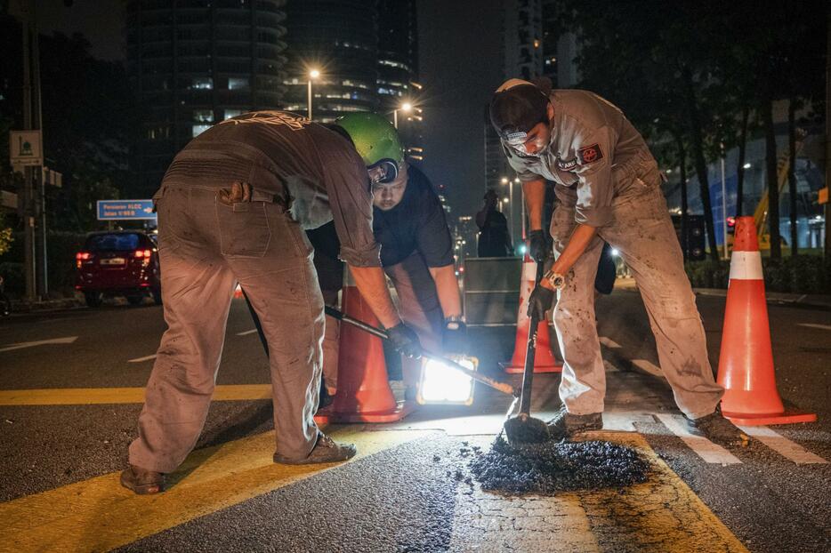 マレーシア・クアラルンプールで道路の穴を修復する勝手連「兄弟」のメンバーら＝2024年4月（共同）