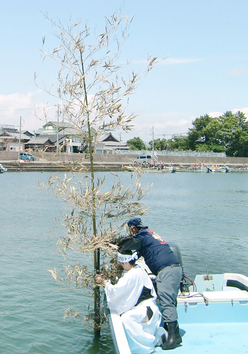 船に乗り、海中に竹を立てる先達の山中さん（左）＝明和町大淀で