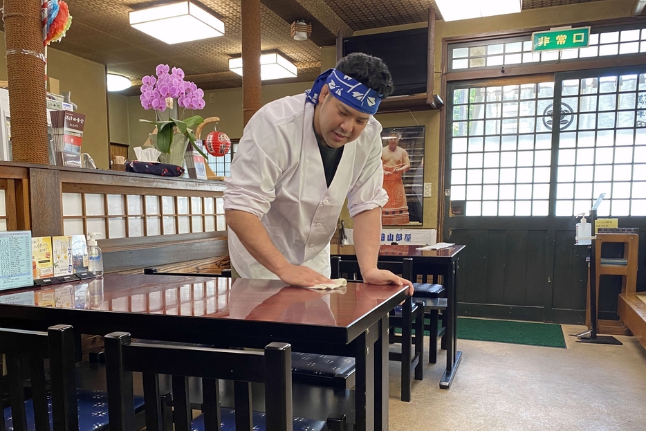 食堂のテーブルを拭く松田さん。店内には力士時代の写真が飾られている
