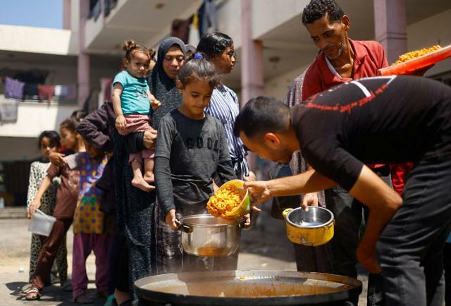 2024年6月26日、パレスチナ自治区ガザ南部ハンユニスで食料を受け取るパレスチナ人=ロイター