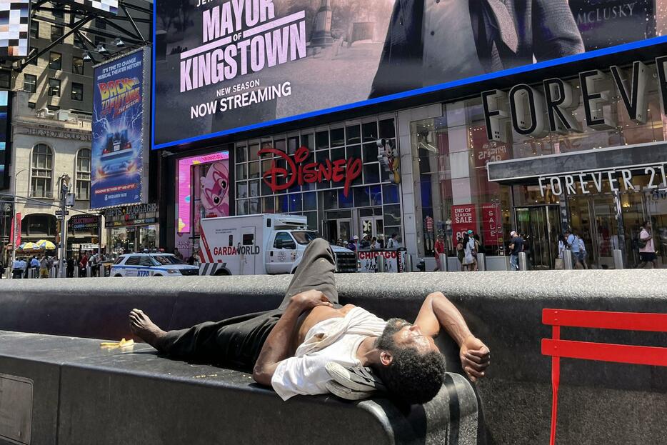 米ニューヨークの繁華街タイムズスクエアのベンチで横になる男性＝21日（共同）