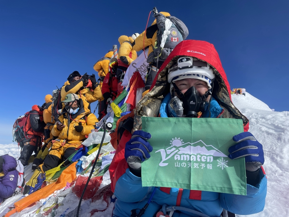 世界最高峰エベレストの頂上付近でヤマテンの旗を持って登頂を喜ぶ猪熊さん（猪熊さん提供）