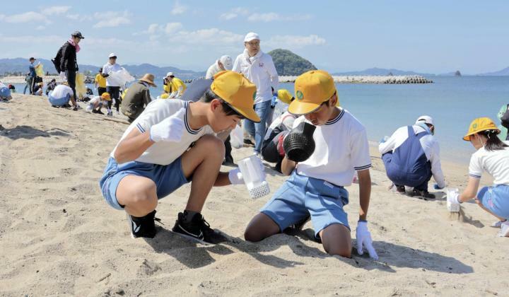 砂に埋まったごみを拾う児童ら＝5日午前、松山市大浦