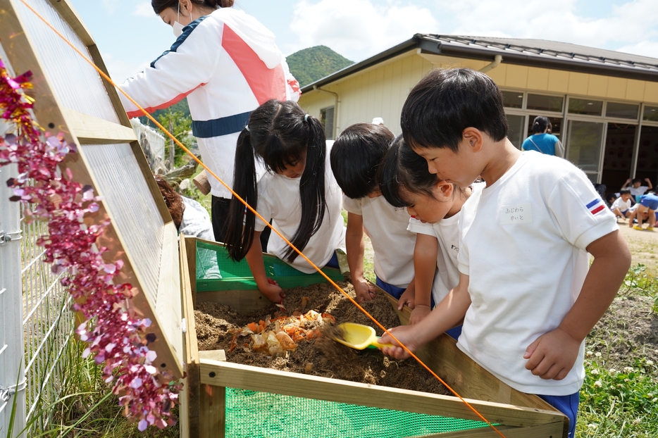 竹チップの土を掘って、野菜くずを埋める園児ら