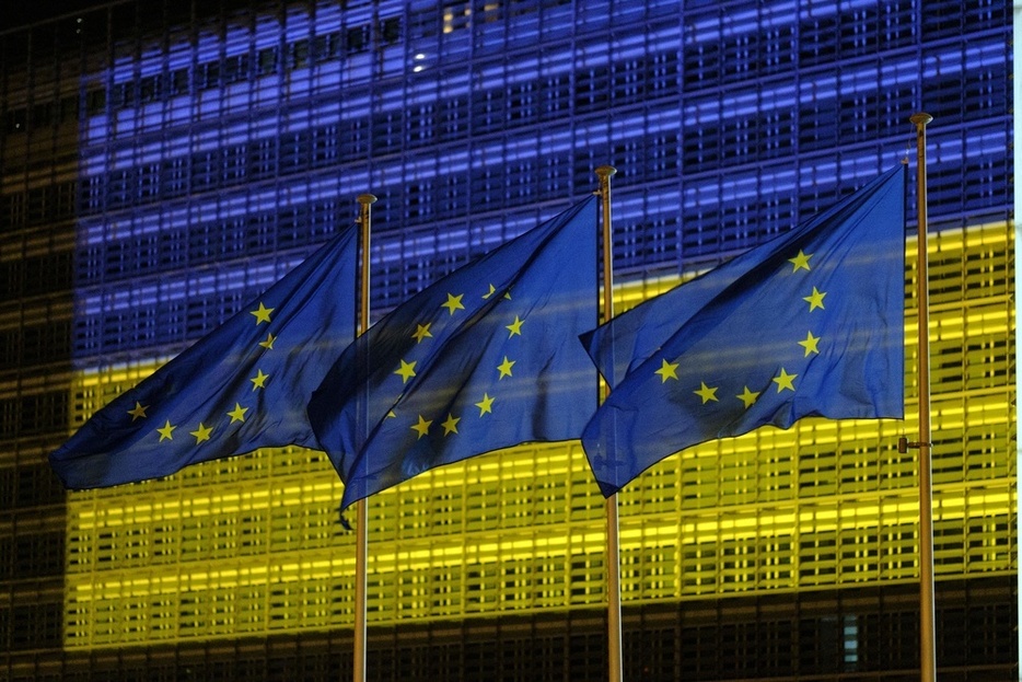 青と黄色のウクライナ国旗の色にライトアップされたEU本部の建物とEU旗＝2022年5月、ブリュッセル（ゲッティ＝共同）