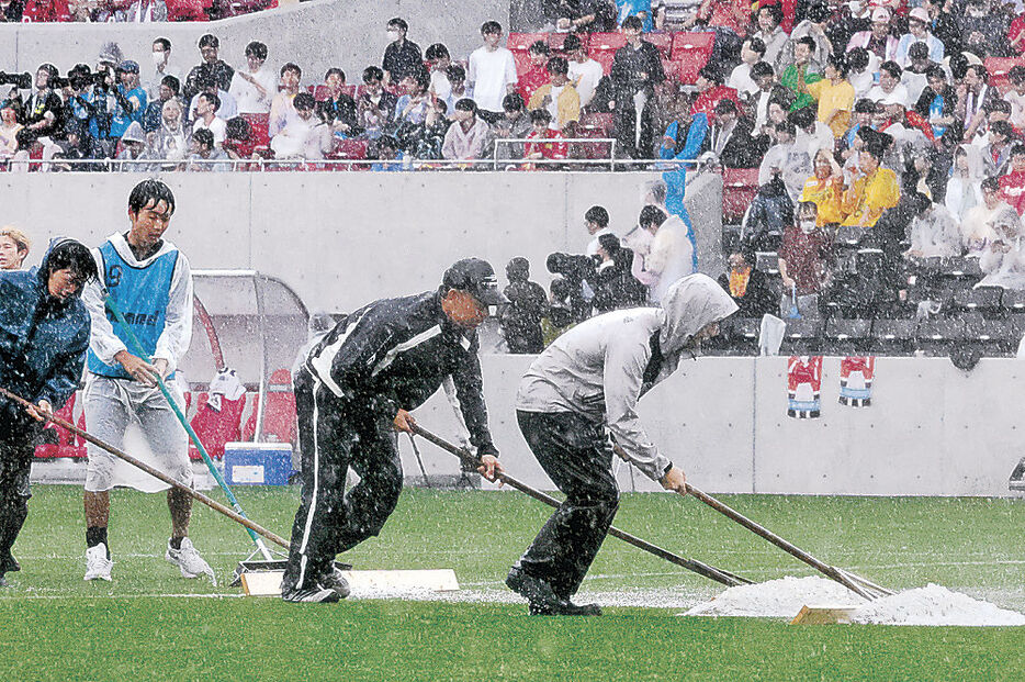 ハーフタイムにピッチにたまった水をかき出す関係者＝２３日、ゴースタ