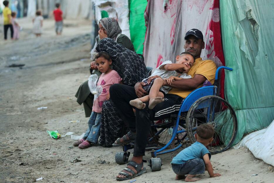 子どもを抱える車いすのパレスチナ人＝15日、ガザ中部デールバラハ（ロイター＝共同）