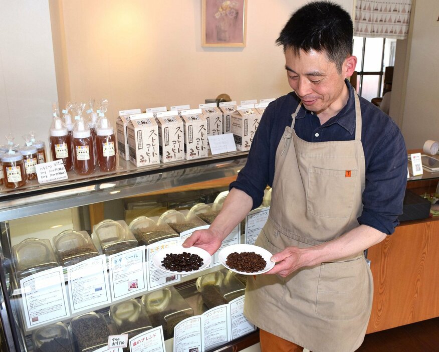 コーヒー豆を手に、仕入れ値の上昇について説明する店長