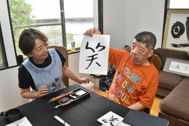 書き上げた作品を敦子さん（左）に見せる和仁さん＝伊豆市