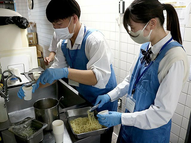 厨房で試食用のラーメンをつくる生徒