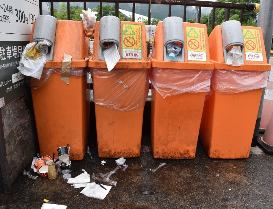 ごみが入れられ、周囲にも紙やプラスチックの容器が散乱するリサイクルボックス＝26日午後、由布市湯布院町川上