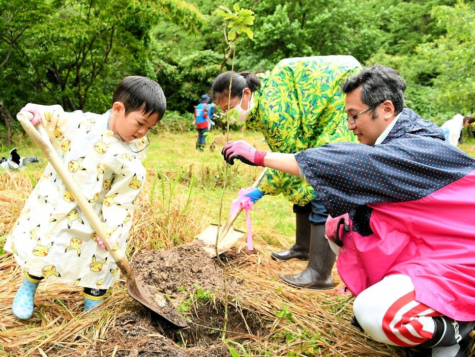 スコップを振るい苗木を植樹する家族連れ＝２３日、三朝町神倉