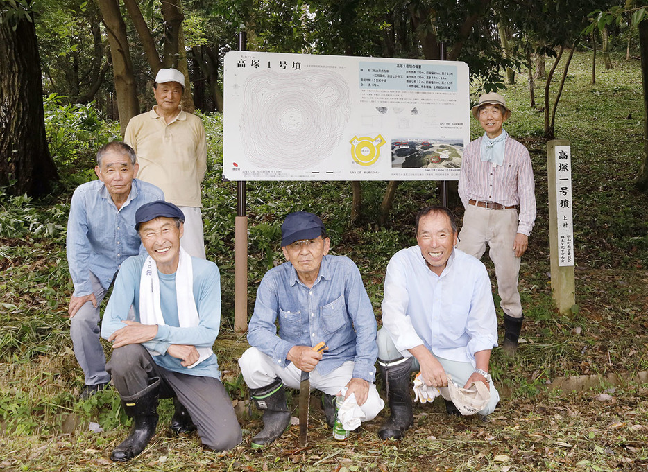 草刈りをして周りがきれいになった説明板を取り囲む明和町郷土文化を守る会の会員たち＝明和町池村で