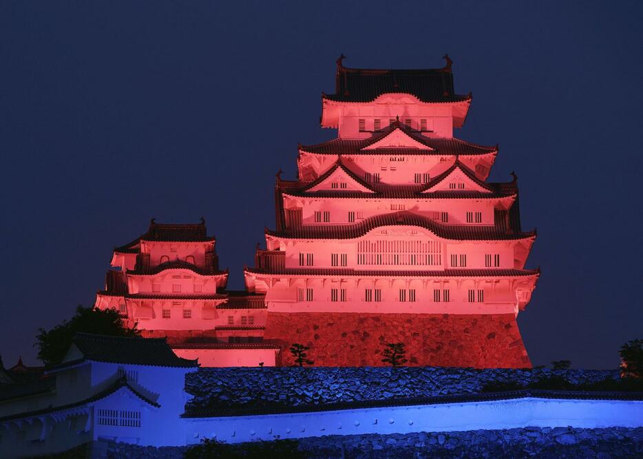 万博開幕まで300日となり、万博のイメージカラーの赤と青色にライトアップされた姫路城＝17日夜、兵庫県姫路市