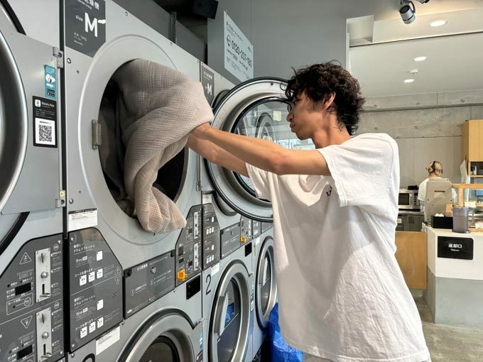 コインランドリーの乾燥機に毛布を入れる男性客＝2024年6月6日、東京都渋谷区