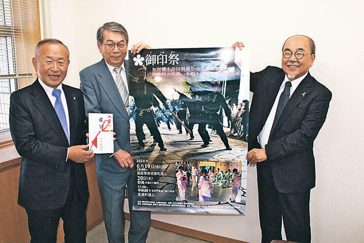 ポスターを手に祭りをPRする（左から）藤田保存会長、鍋谷実行委副会長、山本事務局長=北日本新聞西部本社
