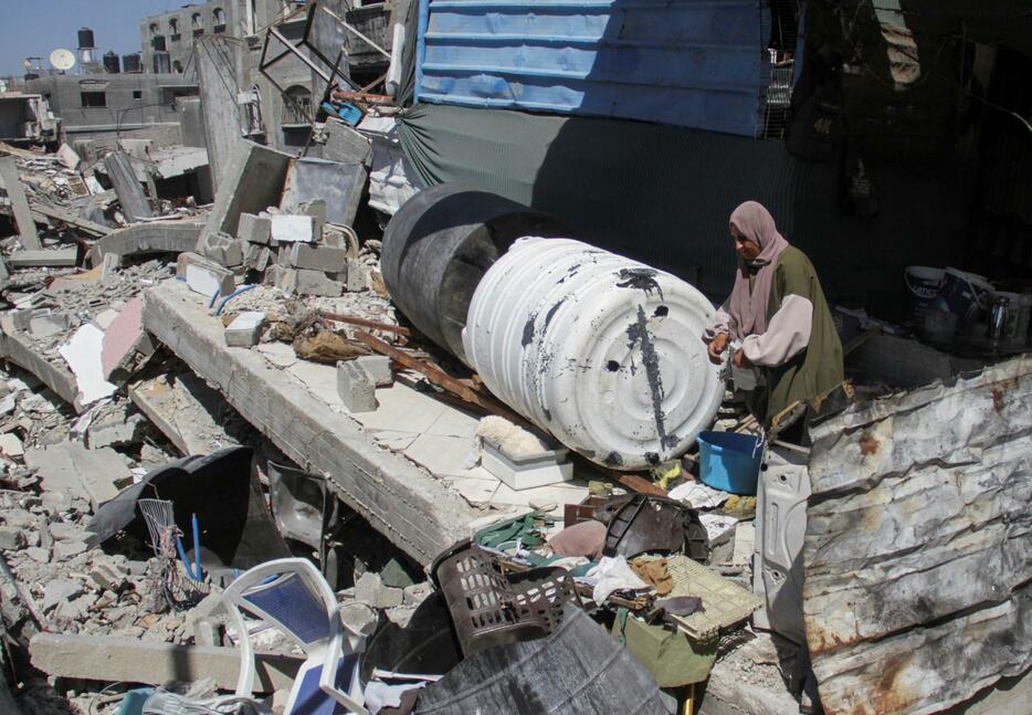 イスラエルの攻撃で破壊された建物のがれきの上に立つ女性＝12日、パレスチナ自治区ガザ北部ベイトラヒヤ（ロイター＝共同）