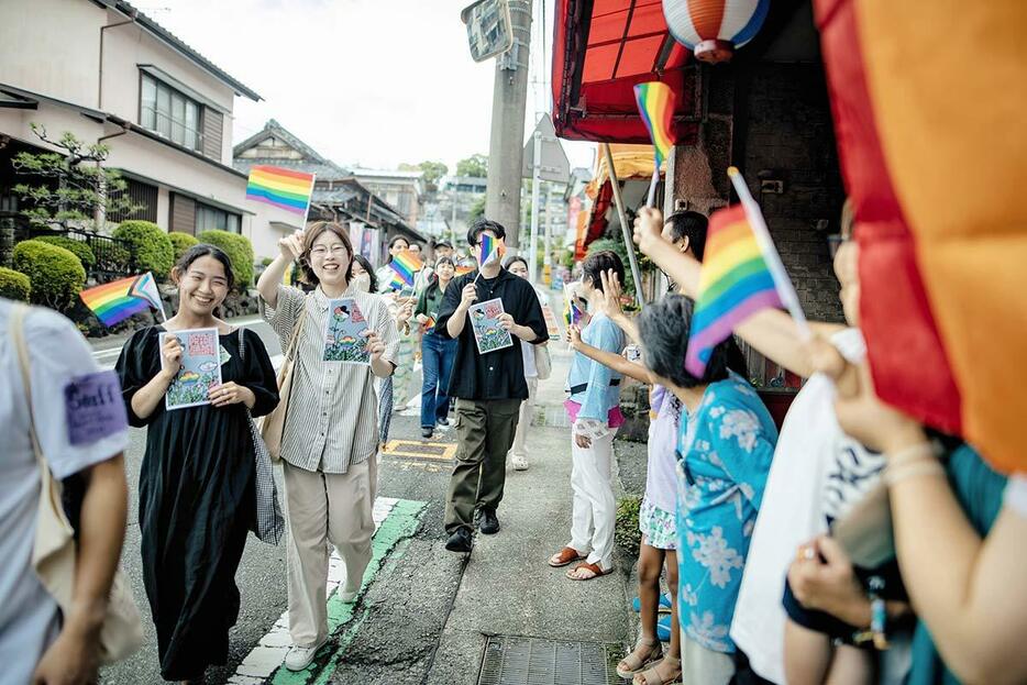 地元酒店「草柳商店」前で、虹色の旗を振りながら歩く「西湘クィアプライド」参加者ら＝３０日、真鶴町真鶴