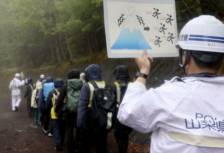 富士山5合目付近で行われた避難訓練で、ピクトグラムを使って参加者を案内する警察官（手前）＝4日午後、山梨県富士吉田市