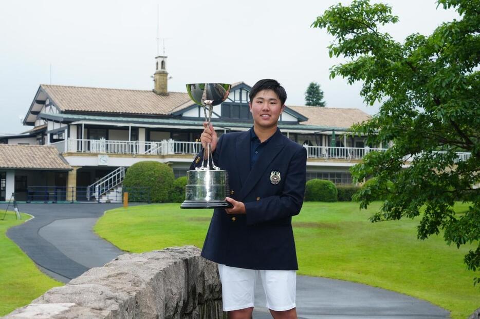 廣野ゴルフ俱楽部のクラブハウスを背に優勝カップを掲げる松山