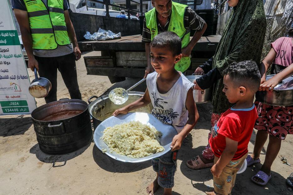 パレスチナ自治区ガザ中部デールバラハで、食事を受け取る人々＝13日（ゲッティ＝共同）