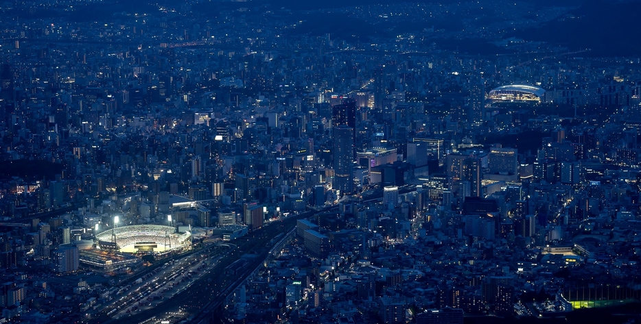 日没後の広島市街地に浮かび上がったマツダスタジアム（手前左）とエディオンピースウイング広島＝奥右（26日午後7時44分）