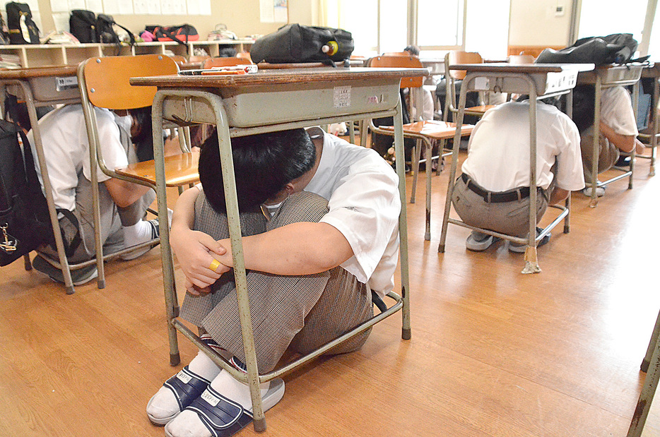 訓練用の緊急地震速報を聞き、机の下で頭を保護する生徒たち＝21日、鹿児島県奄美市名瀬の県立奄美高校