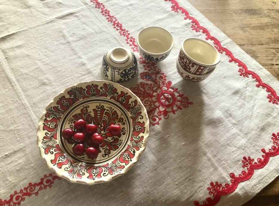 白地に赤や青でルーマニアの伝統的な柄が絵付けされたプレートやカップ。赤い刺繍が目を引くクロスも素敵　PHOTOGRAPH BY YUKARI KOMAKI