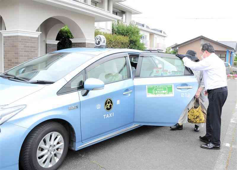 熊本市が19日から北区の植木地域で試験運行を始めたAIデマンドタクシー。病院の前で女性（右から2人目）が乗車した＝19日、熊本市北区