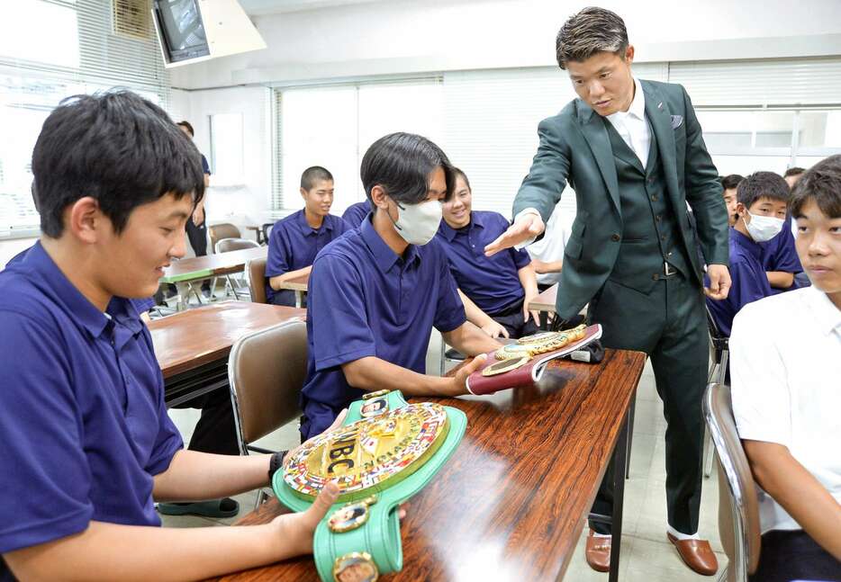 亀田和毅さん（右）のチャンピオンベルトを手に取る生徒たち＝１２日、鹿児島市の鹿児島商業高校