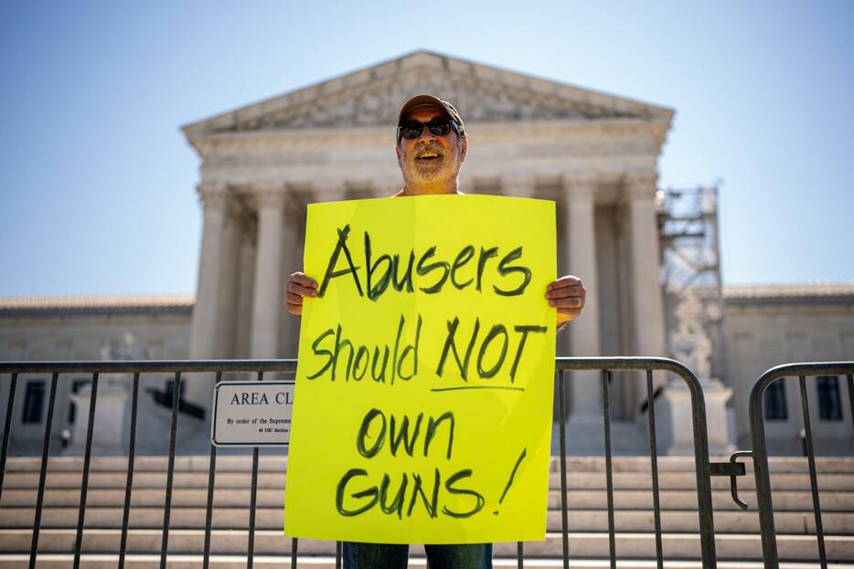 21日、米ワシントンの最高裁判所前で「虐待者は銃を持つべきではない」と書かれたプラカードを掲げる男性（ゲッティ＝共同）