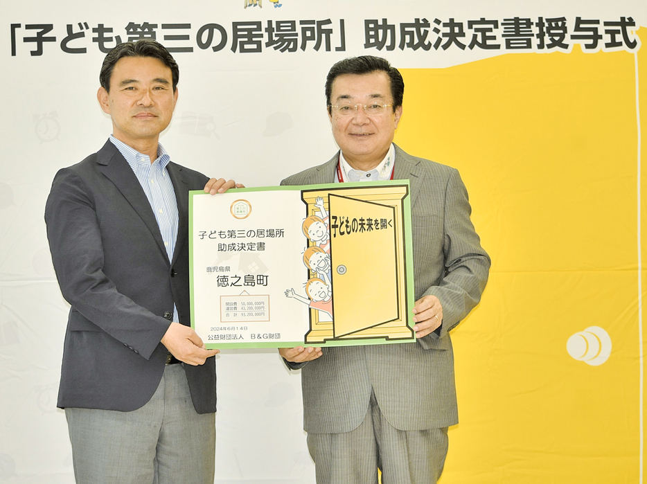 高岡秀規町長に助成決定書を授与する朝日田智昭常務理事（左）＝14日、鹿児島県の徳之島町役場