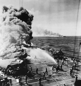 昭和19年10月30日、フィリピン沖で第一神風特攻葉桜隊の突入を受け、炎上する米空母ベローウッド。画面右奥で煙を吐いているのは同じく突入を受けた空母フランクリン