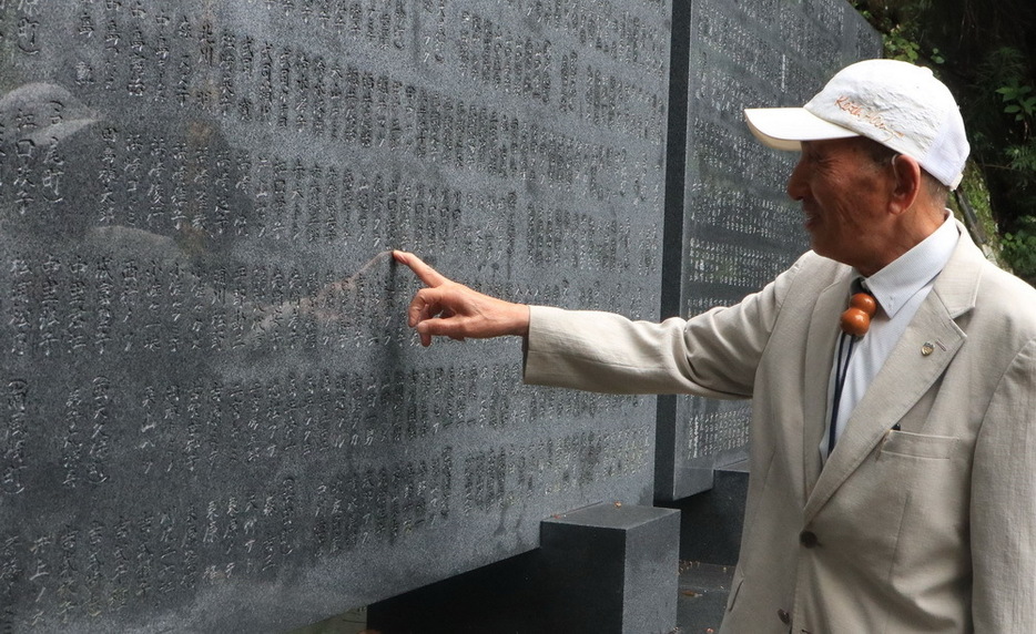 墓銘碑に刻まれた祖父の名前をさすりながら「ここに来ると会えたような気がする」と話す山口さん＝佐世保市、中央公園