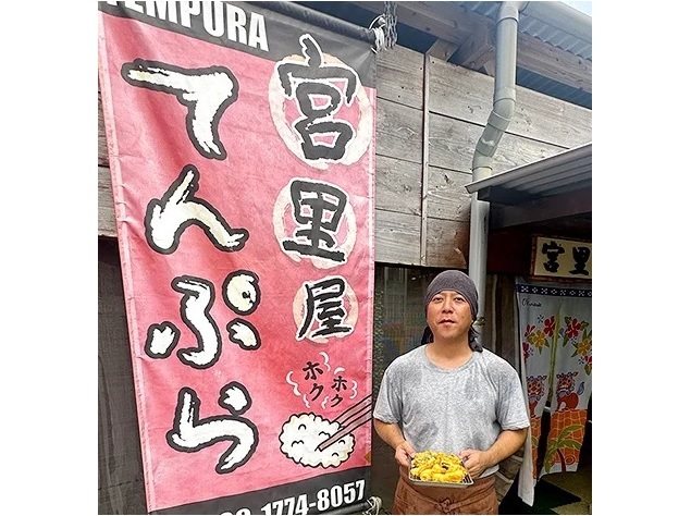 店舗入り口で揚げたての天ぷらを持ち多くの来店を呼びかける店主の宮里さん