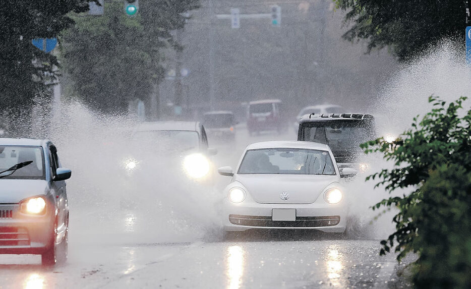 激しく降る雨の中、水しぶきを上げて走行する車＝２３日午後２時、富山市新根塚町