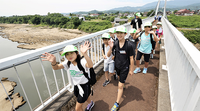 最上川に架かる「竜神の吊橋」を手を振りながら渡る児童たち＝村山市