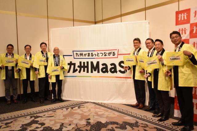 九州ＭａａＳのロゴマークをお披露目しサービス開始をＰＲする河野知事（写真右から４人目）ら＝４日午前、熊本市中央区