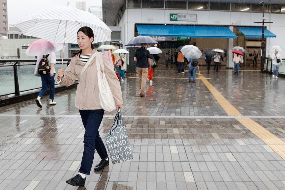 雨の中、傘を手にする人たち＝２１日午後０時半、藤沢駅前