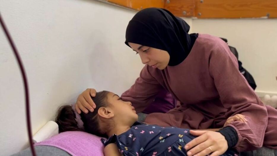 ガザの病院のマットレスに横たわり、母親に頭をなでてもらうヤスミンちゃん