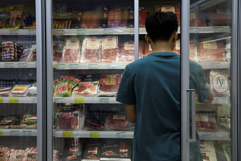 北京のスーパーに並ぶ豚肉などの肉製品と従業員＝13日（ロイター＝共同）