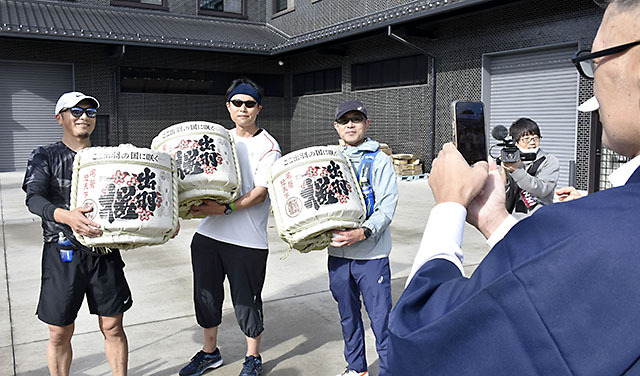 酒蔵や酒販店を巡って開かれた山形酒蔵マラソン。コース上では仕込み水や甘酒が振る舞われ、酒樽を手に記念撮影する人も＝天童市・出羽桜酒造