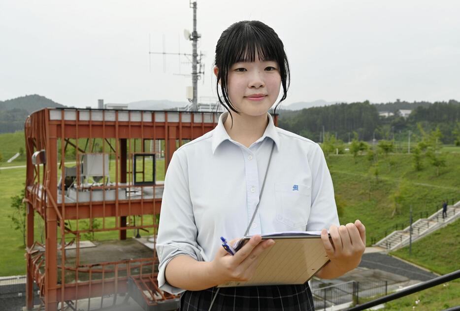 東日本大震災の伝承に力を入れる南三陸高2年の伊藤芽衣さん。奥は宮城県南三陸町の旧防災対策庁舎＝7月