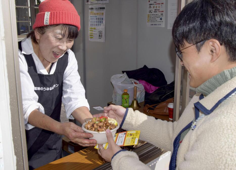 「2024駅長対抗ご当地丼総選挙」で丼を受け取る観光客（右）＝24日午後、北九州市