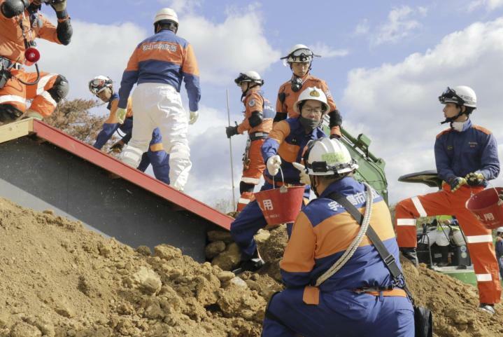 土砂で埋まった家屋から土を運び出す消防団員ら＝24日午前、松山市北梅本町