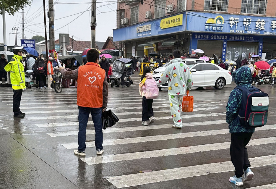 事件があった小学校近くを歩く小学生らと警備に当たる警察官＝20日、中国湖南省常徳（共同）