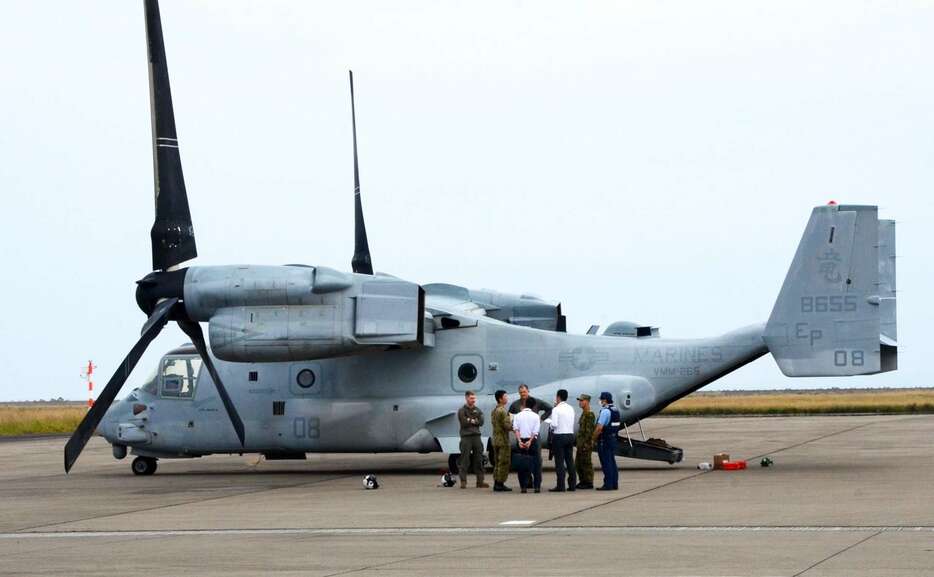 緊急着陸したオスプレイの前で米軍に状況を聞く陸自隊員ら＝１４日、午後２時すぎ、奄美市の奄美空港